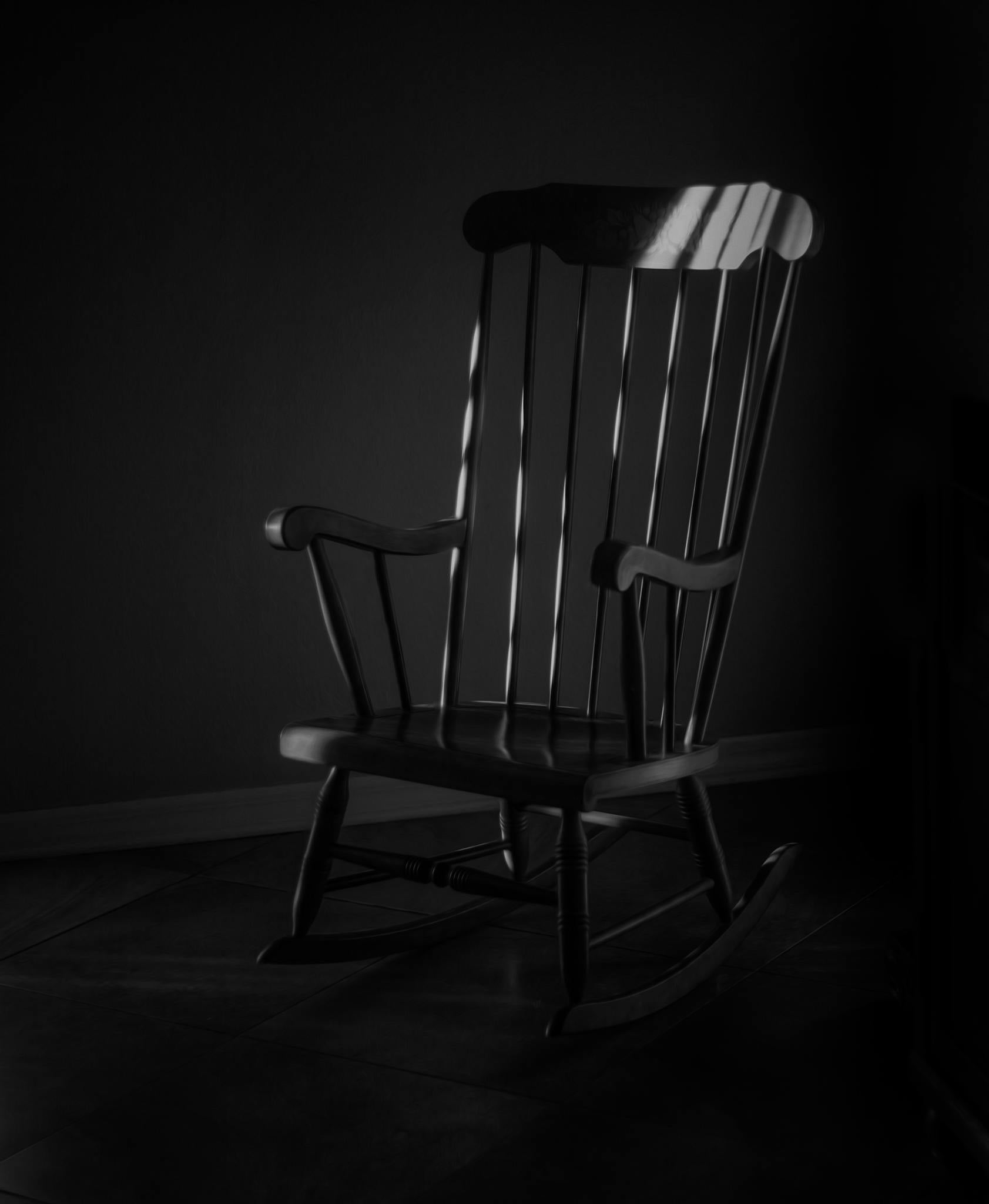 Simple wooden rocking chair with dramatic light and shadow in black and white.