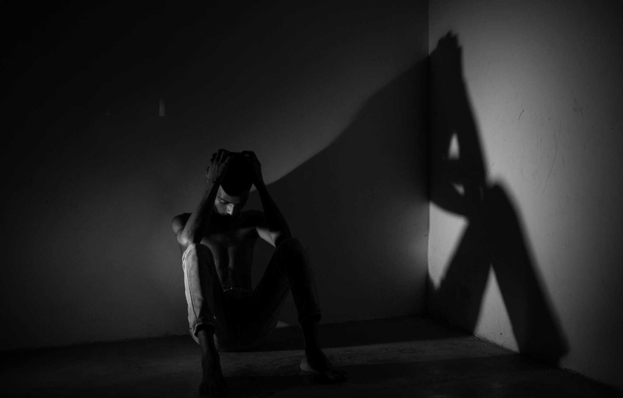 A man sitting in a dark corner with his hands on his head, illustrating deep emotions.